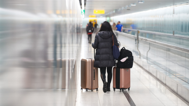 A passenger with luggage walks next to a travelator in a London Heathrow Airport Central Terminal Area.