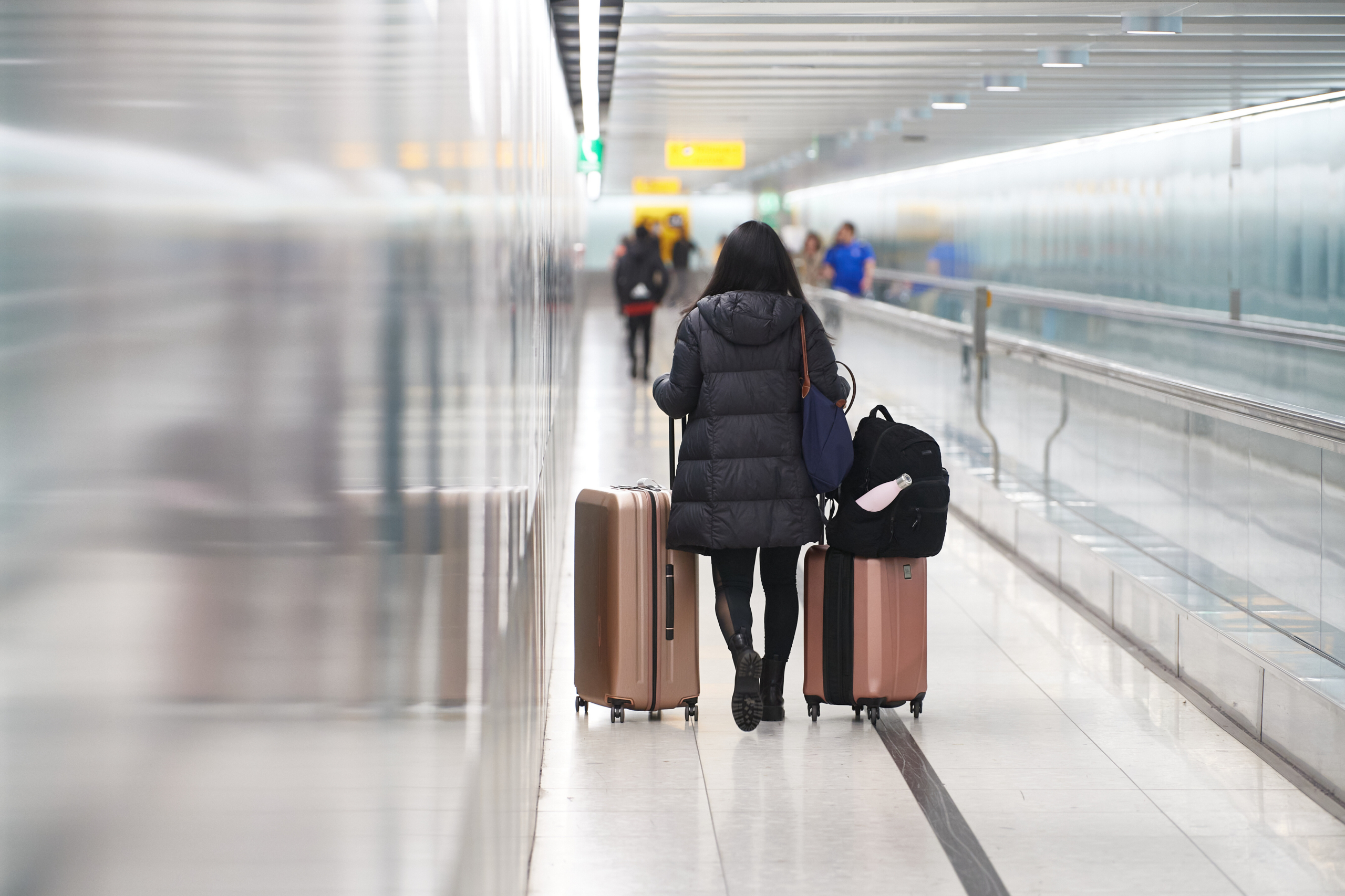 A passenger with luggage walks next to a travelator in a London Heathrow Airport Central Terminal Area.