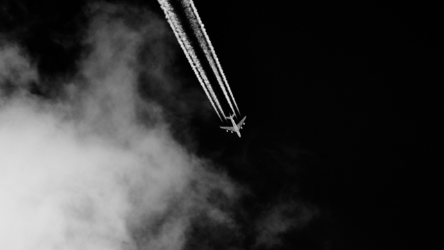 Airplane leaves contrails in the sky with clouds on black background.