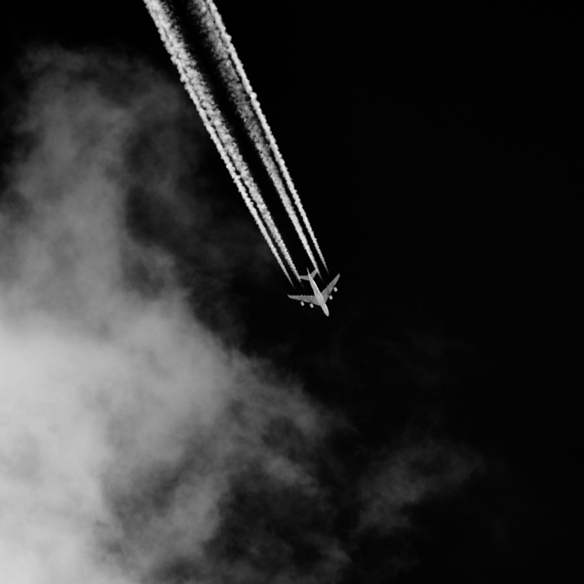 Airplane leaves contrails in the sky with clouds on black background.