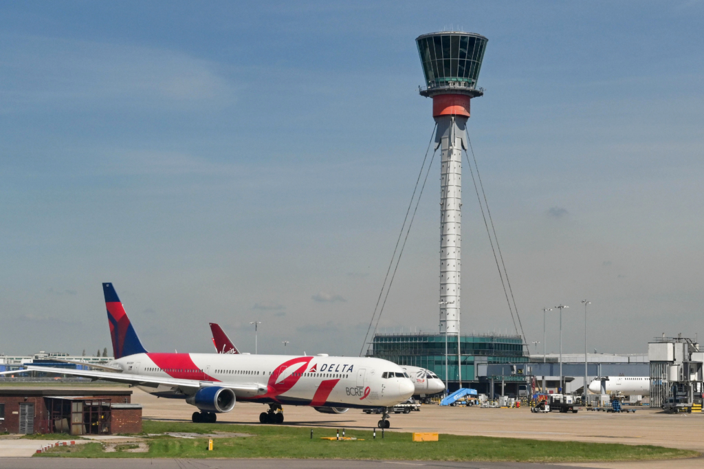 London, England - April 2022: Delta Air Lines Boeing jet with special cancer research paint scheme axiing for take off. In the background is the air traffic control tower.