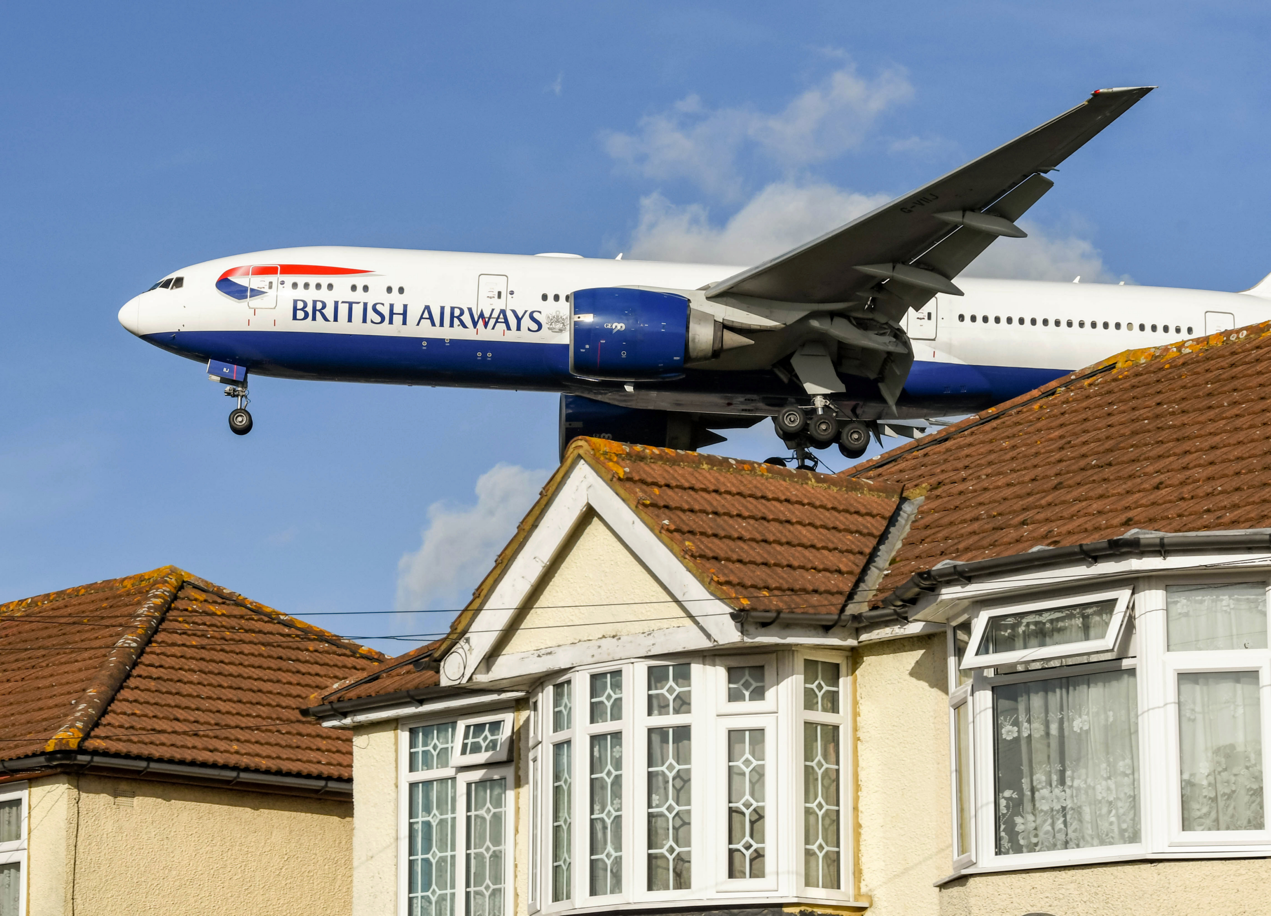 London, England - November 2018: British Airways Boeing 777 jet (registration G-VIIJ) flying low over houses to land at London Heathrow Airport.