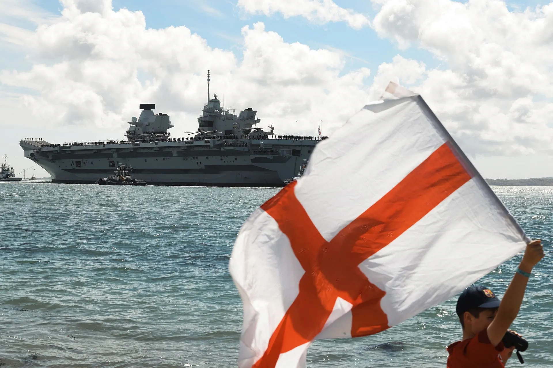 A youngster waves the Flag of St George as HMS Prince of Wales leaves Portsmouth in 2025