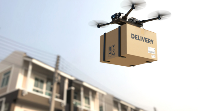 A drone flies with a package on delivery past residential houses.