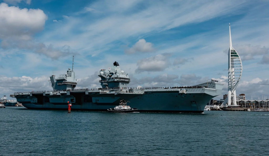 Tugs shepherd HMS Prince of Wales through Portsmouth Harbour as she leaves to begin Op Highmast in A